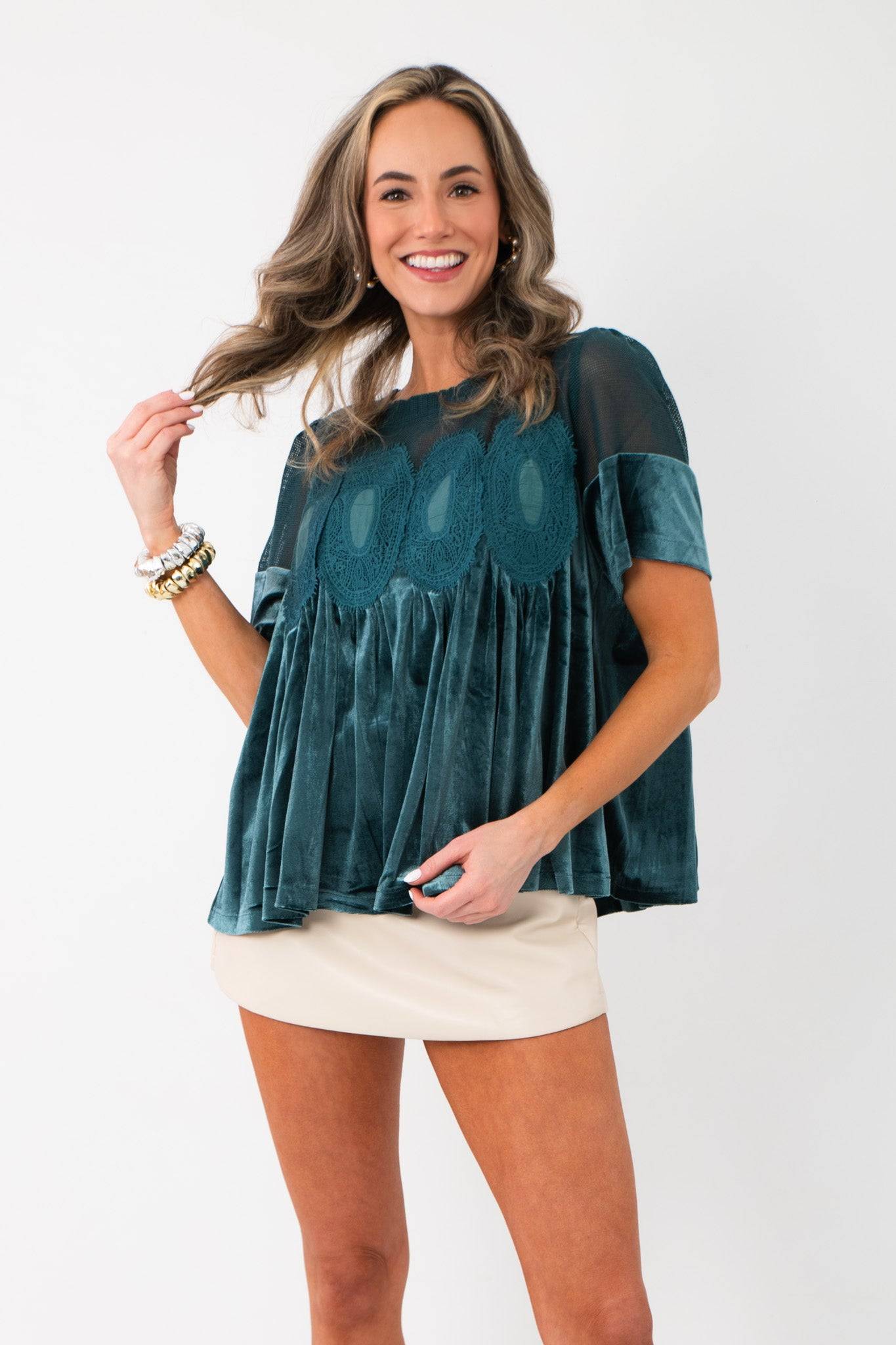 Front view of Lacy Teal Velvet Babydoll Top featuring velvet pleats and lace embroidery, styled with a cream mini skirt for holiday wear.