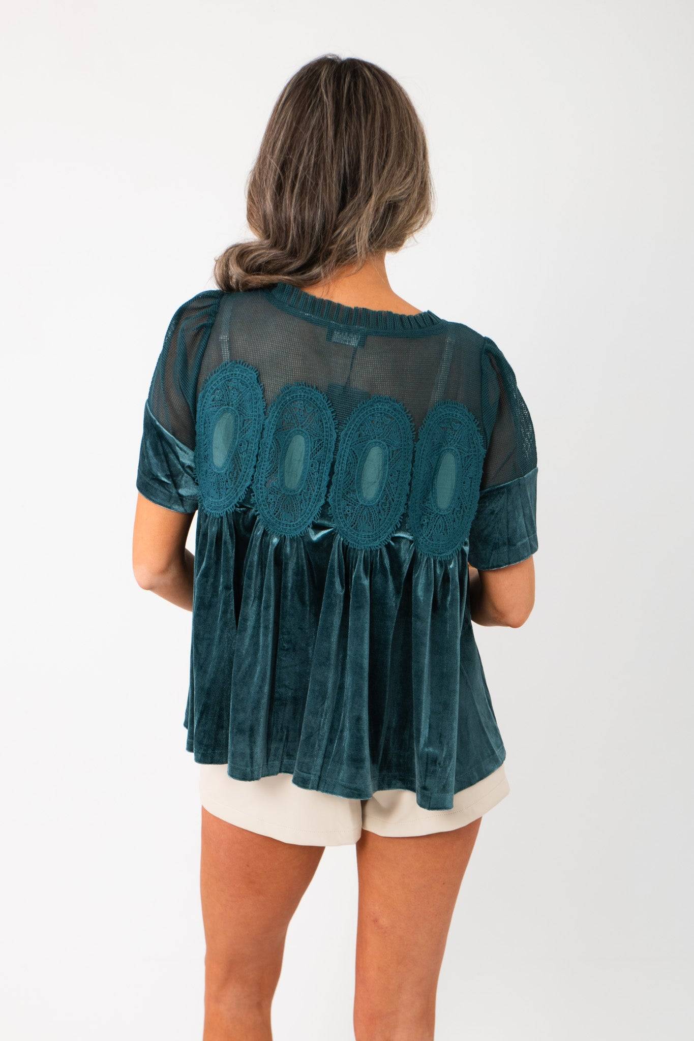 Back view of Lacy Teal Velvet Babydoll Top showing sheer mesh panel and lace detailing, paired with cream shorts for a chic outfit.