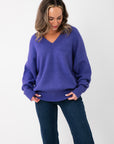 Olivia Oversized Purple V‑Neck Sweater with relaxed fit and ribbed cuffs, styled with dark denim jeans for a cozy fall look.