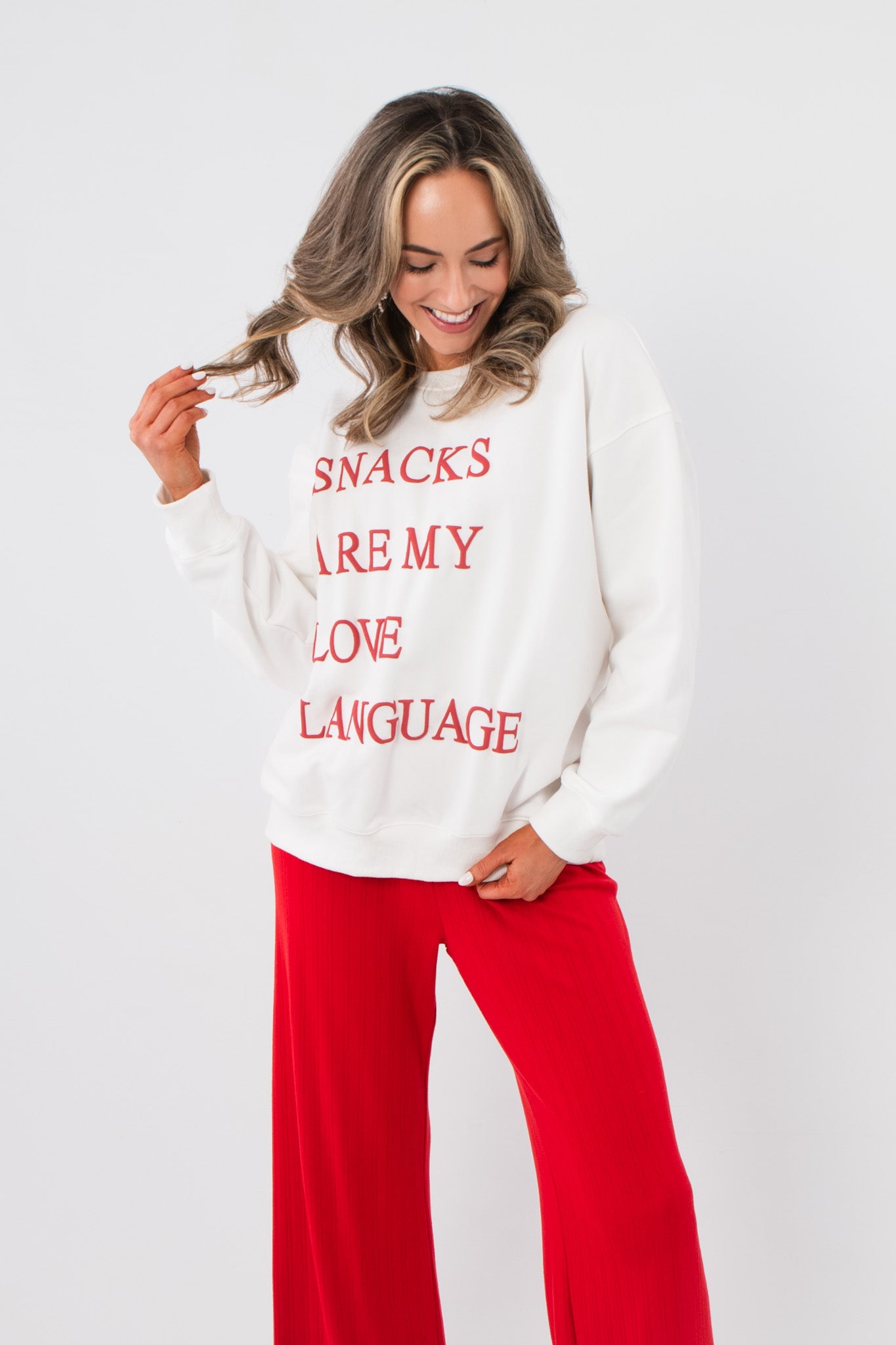 Snacks Are My Love Language Sweatshirt – White graphic pullover with red text, styled with red pants for a cozy Valentine's look.