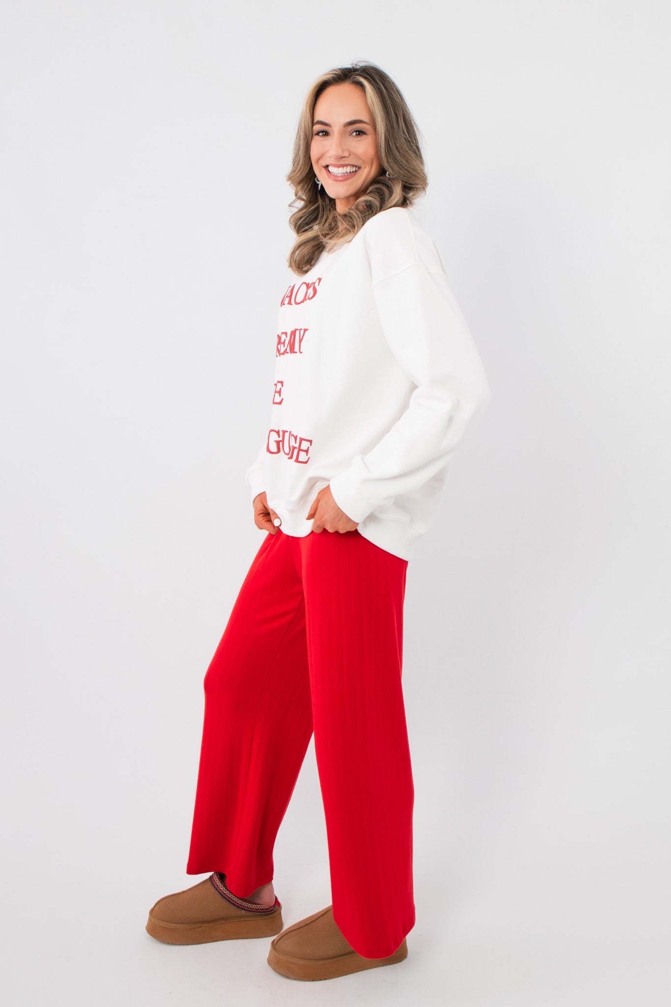 White graphic Snacks Are My Love Language Sweatshirt with red lettering, shown in a side pose with red wide-leg pants.