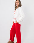 White graphic Snacks Are My Love Language Sweatshirt with red lettering, shown in a side pose with red wide-leg pants.