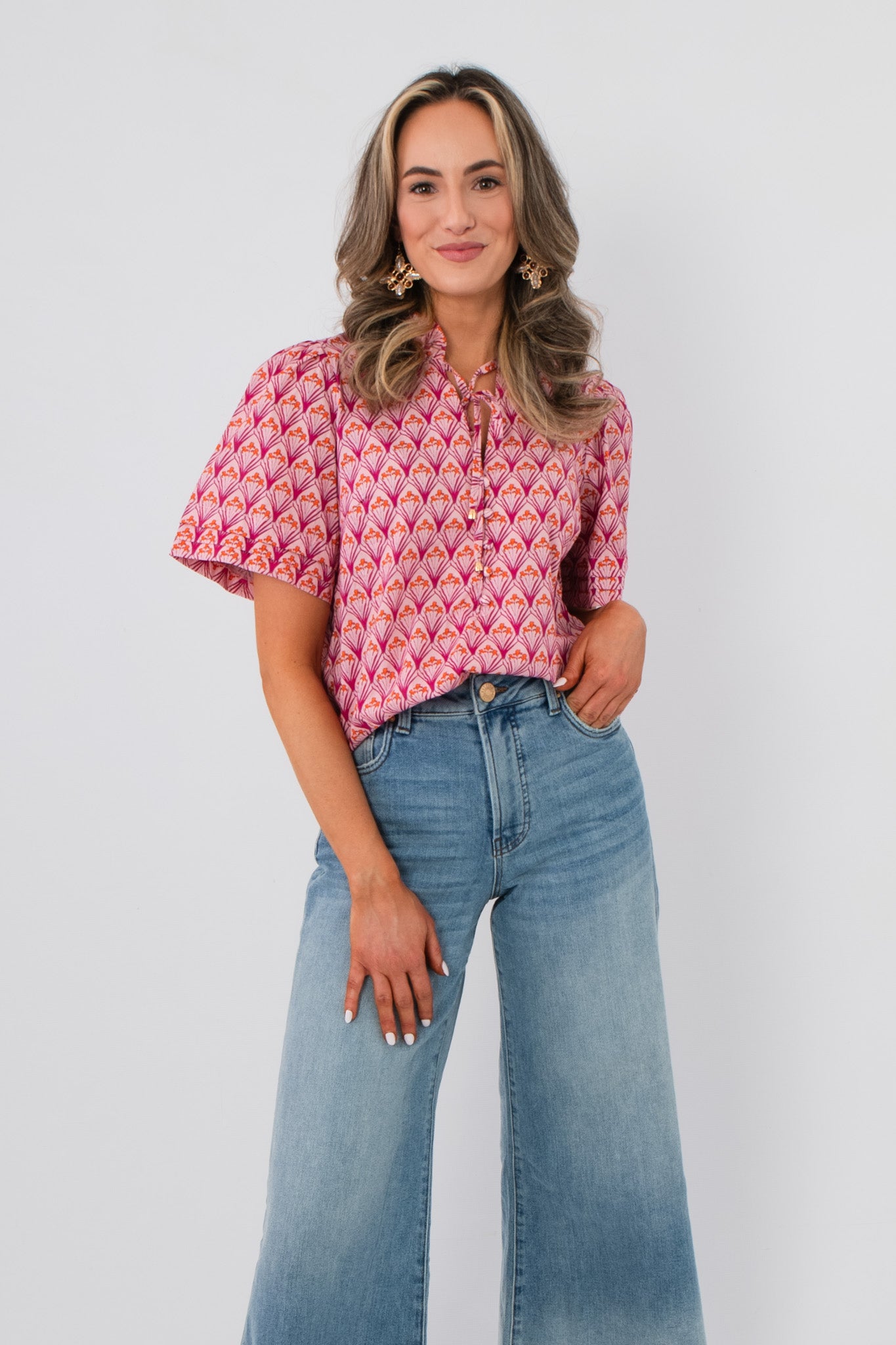 Kallie Pink & Orange Floral Blouse with tie neck and short sleeves, styled with high-waisted wide-leg jeans for a chic spring look.