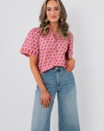 Kallie Pink & Orange Floral Blouse with tie neck and short sleeves, styled with high-waisted wide-leg jeans for a chic spring look.
