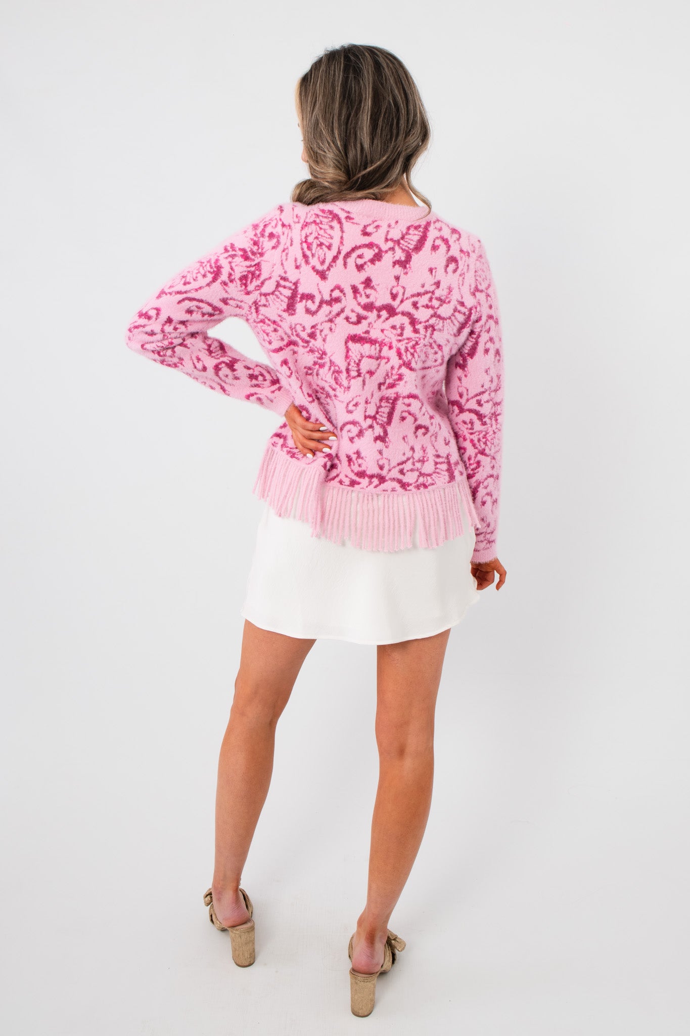 Back view of the Something Sweeter Pink Jacquard Fringe Hem Cardigan highlighting the jacquard pattern and fringe hem over a white skirt.