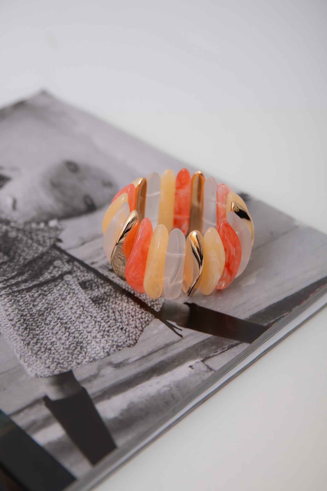 Stretchy Orange Wide Stone Bracelet resting on fashion magazine, highlighting bold summer colors and gold detailing in statement jewelry design.