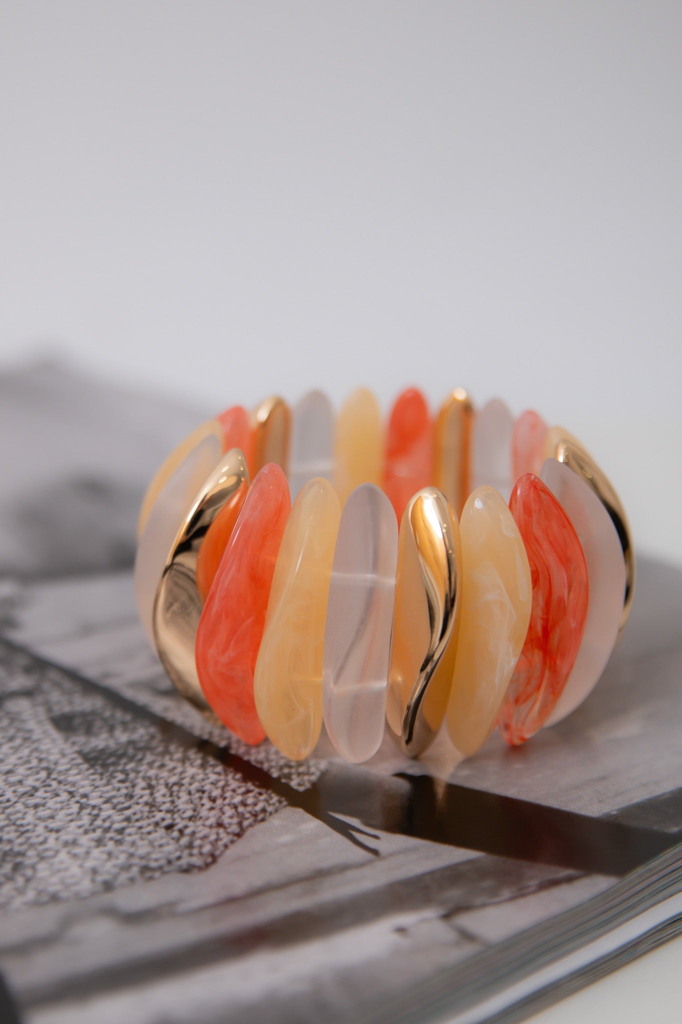 Orange Wide Stone Bracelet displayed on magazine, showcasing multi-color stones in orange, peach, and frosted tones with gold accents.