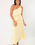 Andie Yellow Layered One Shoulder Maxi Dress styled with a gold clutch, ideal for weddings, parties, or vacation occasions.