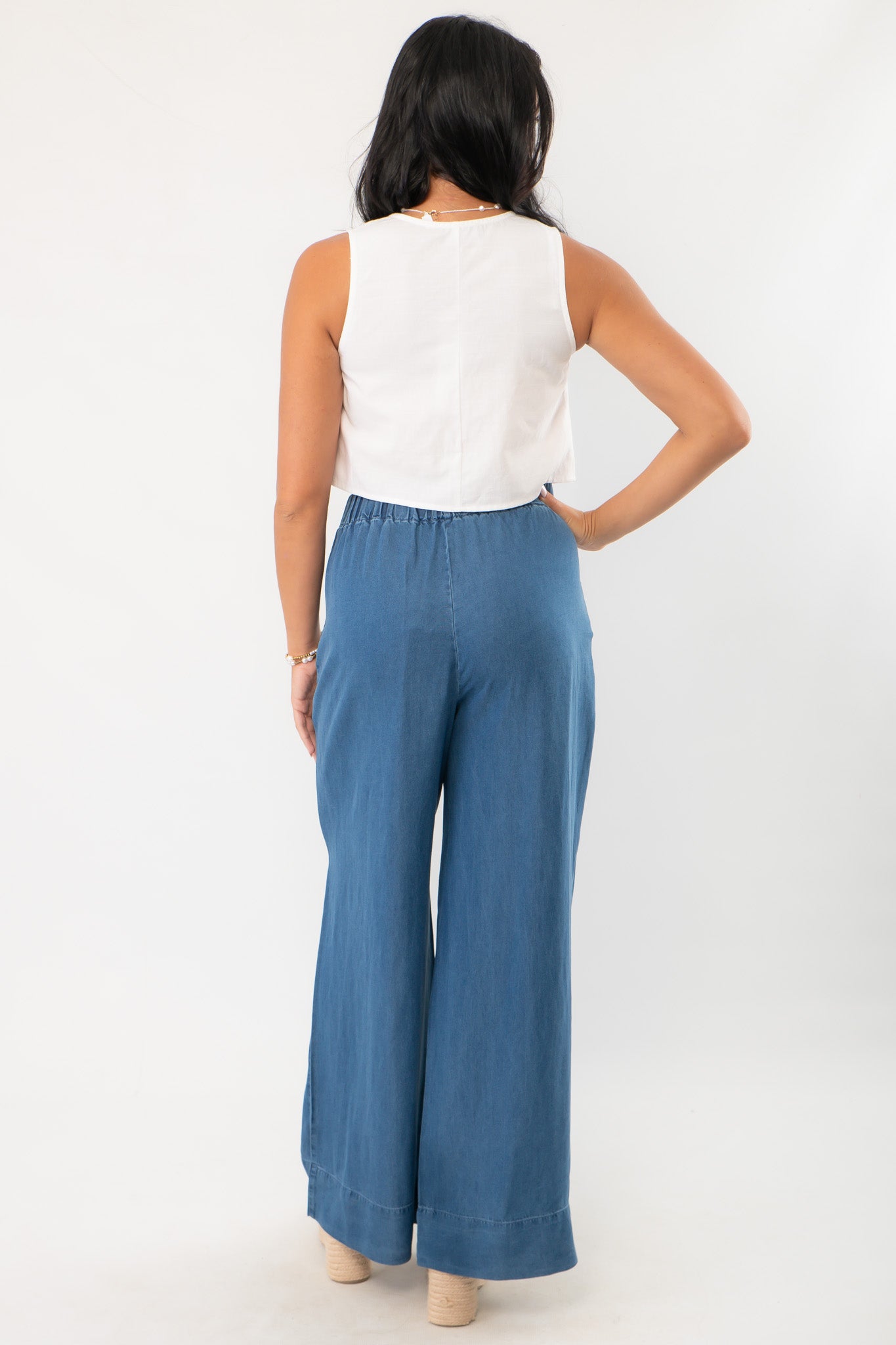 Back view of MinkPink Isadora Embroidered Top showing clean white sleeveless design, paired with wide-leg blue pants.