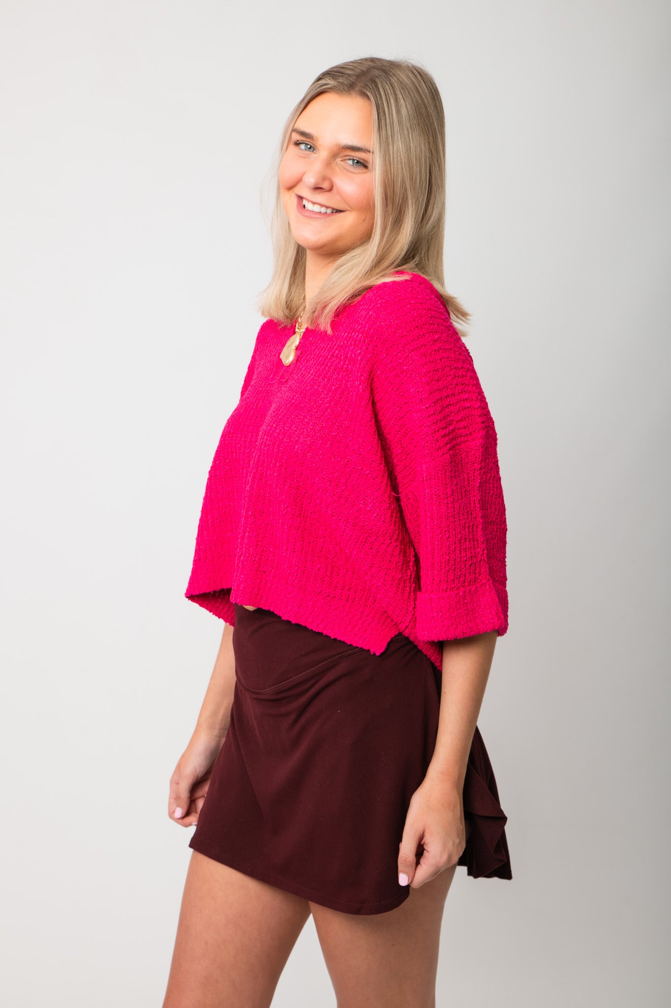 Side view of Fuchsia Short Sleeve Crop Sweater – Oversized pink knit top with relaxed fit and short sleeves, paired with a burgundy skirt.