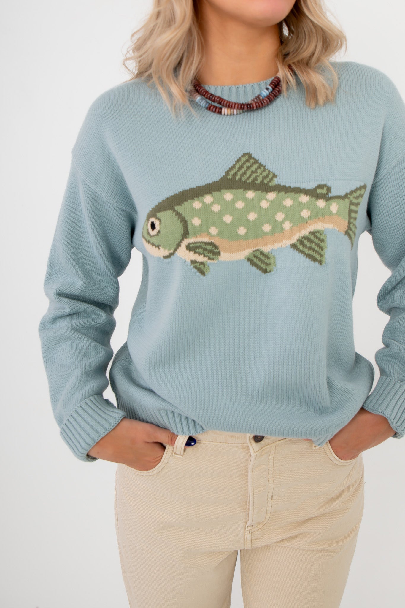 Person wearing a light blue sweater with a fish design on a plain background