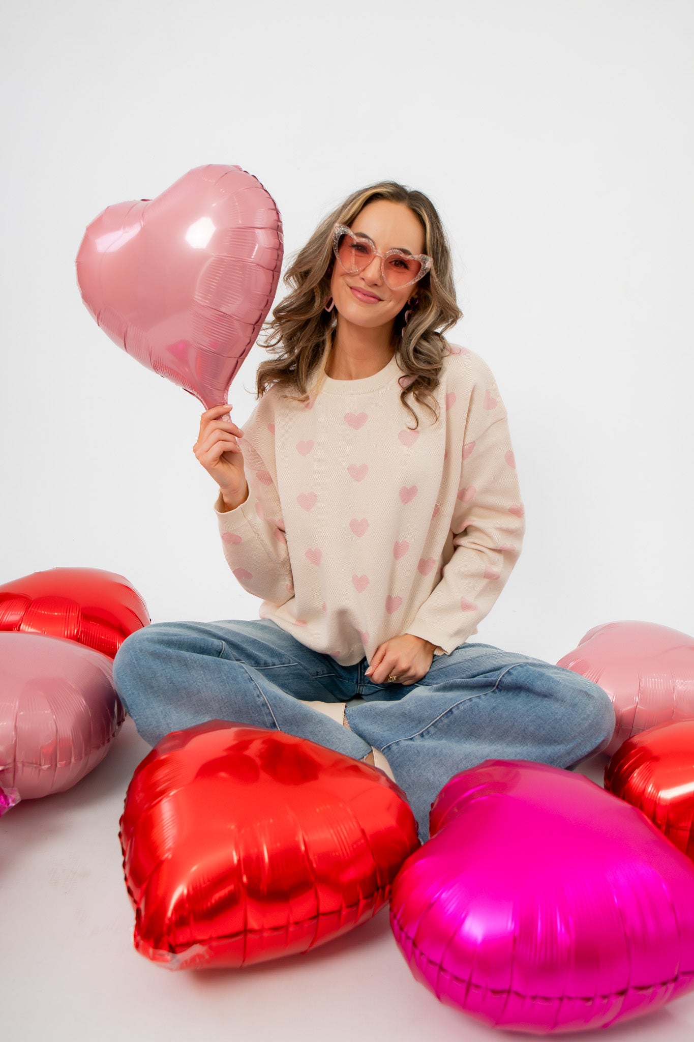 Woman holding a heart-shaped balloon surrounded by more heart balloons on a white background